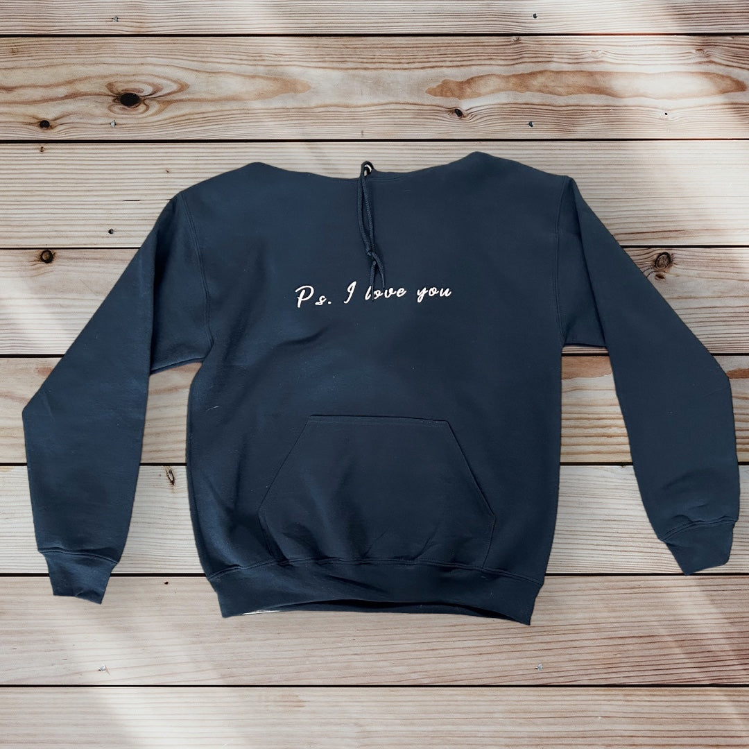 PS I Love You Mental Health Hoodie - a black hoodie with white text that reads PS I Love You.  The hoodie is on a brown wood background